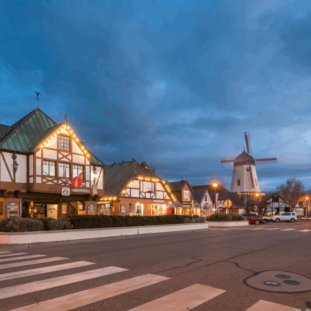 Colorful small town with carousel, windmill, and quaint shops illuminated at dusk.